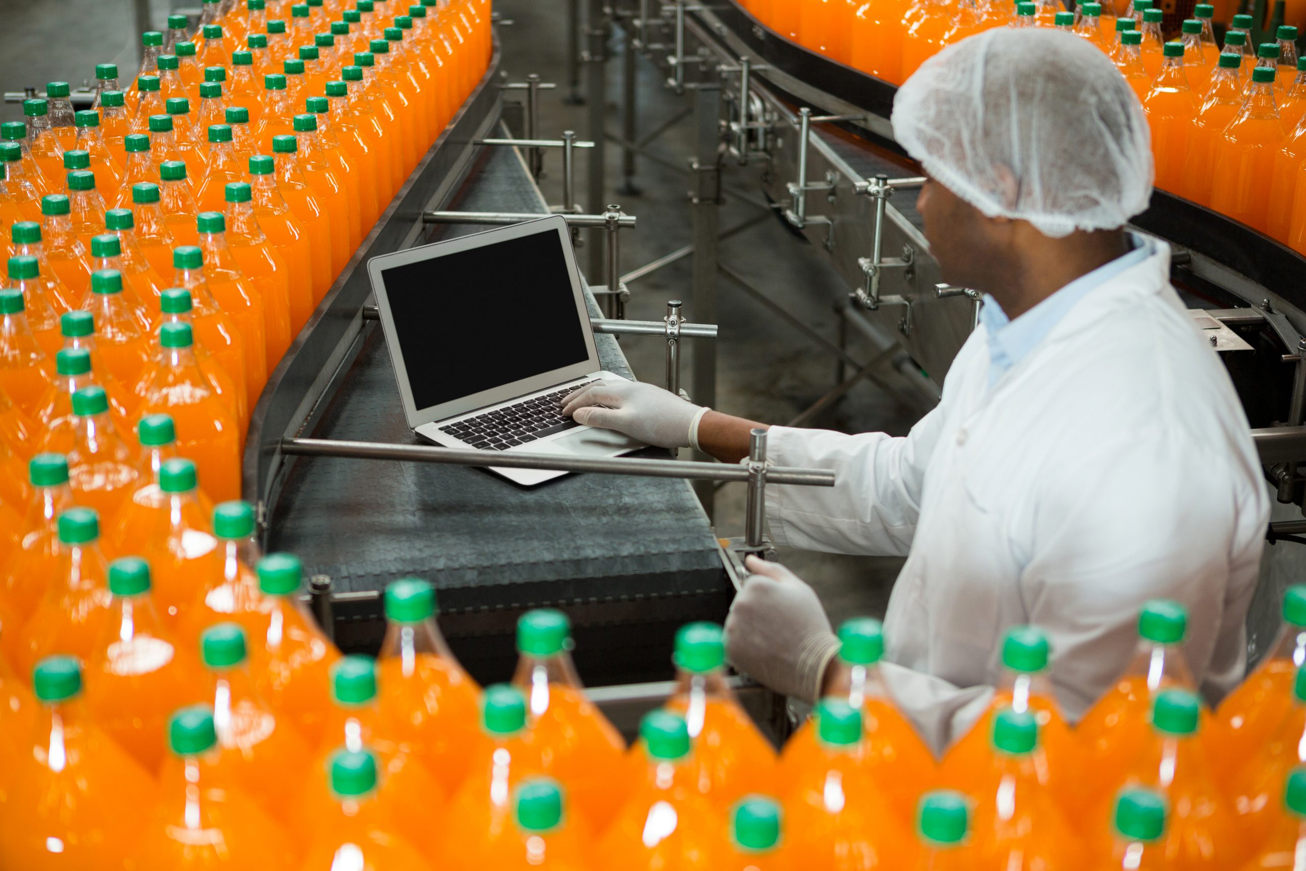 male-worker-using-laptop-amidst-production-line-juice-factory